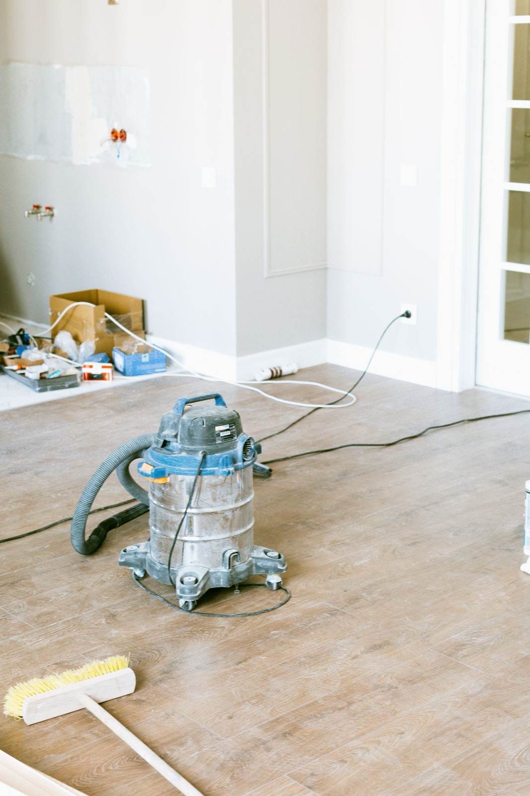Shop vacuum and broom clearing construction dust from a freshly finished floor after drywall and paint